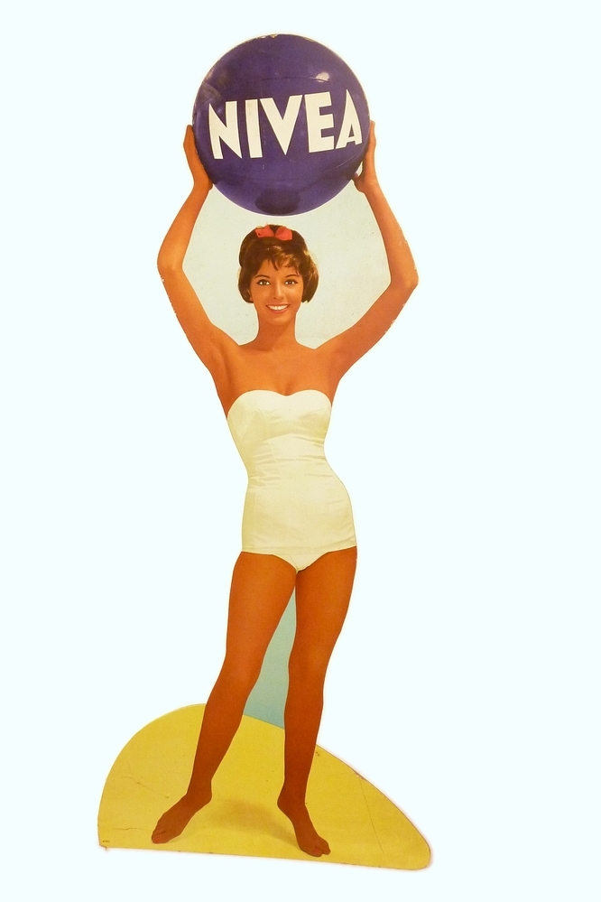 kartonnen plaat in de vorm van een vrouw in badpak die een blauwe bal boven haar hoofd houdt met daarin in wit nivea
