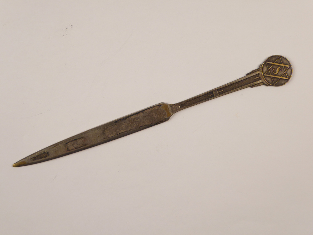 langwerpige spitse verzilverde messingen briefopener met op uiteinde decoratie S in ster, aan achterzijde gegraveerd W.A.Scholten's aardappelmeelfabrieken Groningen (Holland)