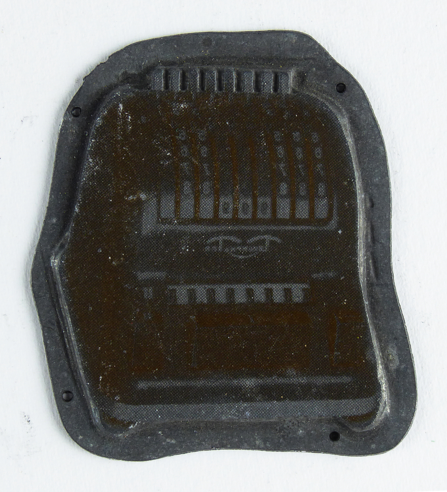 grillig gevormde non ferro metalen cliche met afbeelding tel- of rekenmachine, afkomstig van kantoorinstallaties Bv Schuur te Veendam, achterkant olijfgroen