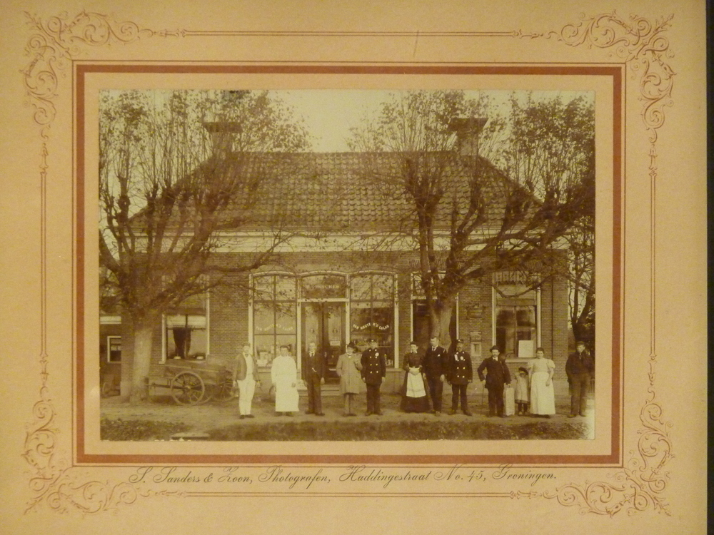 een aantal personen staan voor een winkel met opdruk ? Bosscher, links voor staat een ventkar met opdruk Brouwerij Voorintholt Bosscher, aan de muur een bord hulpkantoor der posterijen. achterop tekst op papier:  op de foto van L naar rechts schilder voorintholt,  slager keizer, kruidenier M Brouwer, koren koopman G Koning, postbode Weling, mevr Brouwer, postbode Gerringa, Simon v.d. Pool, laatste 2 + kinderen vermoedelijk schippers fam