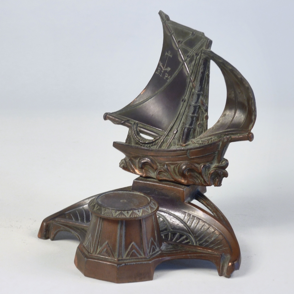 gebronst koperen inktstel als versiering een eenmastschip met bolle zeilen. In het grote zeil is een anker gegrift, waaronder de letters B.I.P.1. Het glazen inktpotje ontbreekt