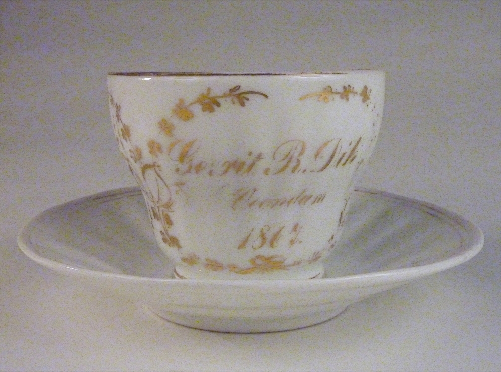 porseleinen kop en schotel met goudkleurige inscriptie Gerrit R Dik Veendam 1857. Waarschijnlijk gaat het hier om een jubileumkop, ter gelegenheid van het 10 jarig huwelijksjubileum van Gerrit Roelof/ Roels Dik en Johanna Hinderika Duintjer, getrouwd op 11-02-1857 te Veendam.
Gerrit Roelof/ Roels Dik, geboren 19-03-1830 te Veendam, als zoon van Roeld/ Roelof Pieters Dik, schipper en Aagtje Pieters Muntendam.
Gerrit Roelof/ Roels Dik was o.a. schipper in 1857, 1859, 1862, 1863, 1877, in 1877 overleden aan boord van een schip.