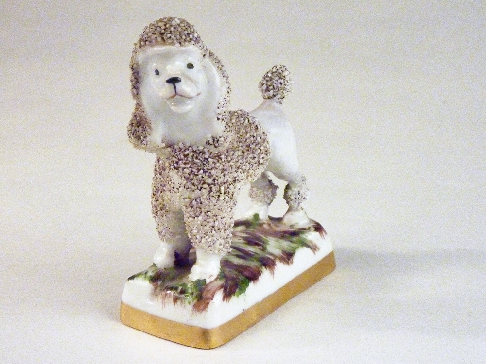 witte steengoed poedel met donkere lichaam van gruis, staand op een ondergrond van bruin en groene vegen, staand op een witte plateau met gouden rand.