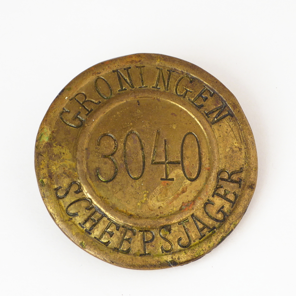 ronde messing scheepsjagerspenning, met op voorkant geslagen inscriptie Groningen 3040 Scheepsjager. Scheepsjagerspenning afkomstig van Jan Prins, 43 jaar  te Winneweer. Schenker zijn grootvader, Willem Kuiper, geboren 2 juli 1888 te Wedde kocht deze scheepsjagerspenning en droeg deze. Willem Kuiper, geboren 2 juli 1888 te Wedde als zoon van Harm Kuiper en Ottje Houwing, huwde (1) op 9 november 1912 te Bellingwolde met Ida Hulsing, huwde (2) op 31 mei 1919 te Bellingwolde met Maria Lammers. Hij was arbeider, turfsteker.