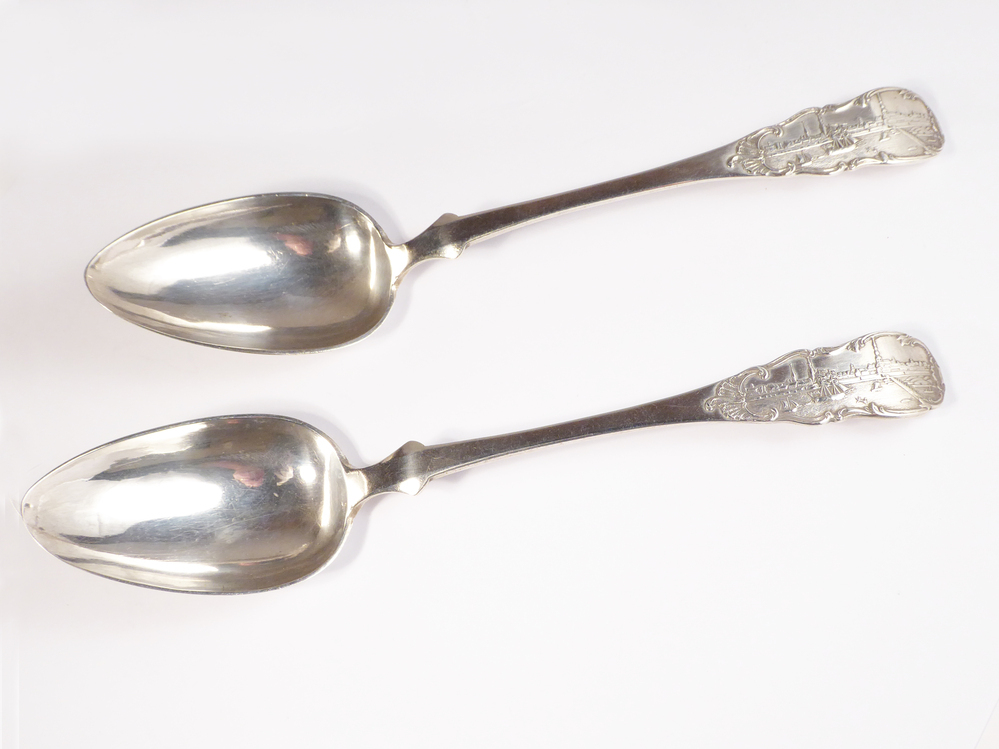 2 zilveren oostzeelepels, op uiteinde steel gedreven voorstelling van de haven van Riga met gebouwen en zeilboten, onderkant overgang steel bak heeft een lofje, onderkant uiteinde steel gegraveerd : F.M. Schultz d. 13 April 1849 A.B. , meesterteken AW = Johann Adolph Emanuel Wittenburg. Geboren 15 december 1813 te Riga als zoon van goudsmid Johann Christiaan Wittenburg. Van 1828 - 1833 in de leer als goudsmidsgezel bij zijn vader in de werkplaats. Sinds 12 januari 1839 meester, van 1857 - 1865 olderman. Trad op 11 juli 1872 uit het ambt en werd tolambtenaar bij de bruggen. Overleed 5 maart 1889. Essayeurmerk omgekeerde V III (russische schrijfletter L S = Leopold Schlütter 1845 - 1849), jaartal 1849, gehalteteken 84, stadskeur Riga, 2 figuurtjes naast een torentje met bovenin een kruis.