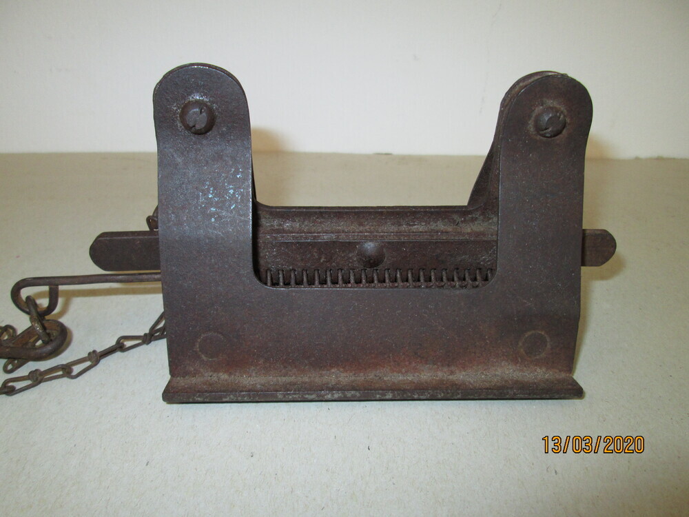 Omgekeerde V vormige ijzeren voorwerp, met verdikte onderkant, waarvan de onderkant haaks is omgebogen tot een rand van 2 cm, 12 cm lang, 6 cm hoog, in het midden tussen de zijkanten hangt een 17 cm lange staaf met daaraan 32 krammetjes, afwisselend hoog en laag gehangen, welke in het oogje aan de bovenkant geborgen zijn door een lange metalen pen, hangende aan een ketting aan de voorkant. Het is een platteriemklem, gebruikt om aandrijfriemen te repareren. Vanwege de grote oren in het Drents ook wel een ‘kniene ‘genoemd. Hoe het werkt: je zet het in de bankschroef, en een kaartstrookje krammen erin en de pen weer door die krammen, dan platte aandrijfriem erin tussen de krammen ,de bankschroef aanklemmen en de krammen zitten in de riem. Dit aan beide kanten van de riem, een soort pees erdoor , en je hebt een aandrijfriem. En de riem was altijd aan te brengen zonder dat je eerst nog lagers of iets dergelijks moest verwijderen. Volgens schenker waarschijnlijk afkomstig van een aardappelzetmeelfabriek.