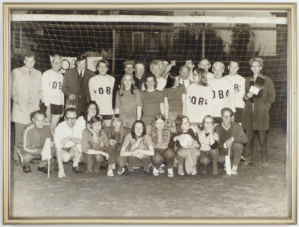 groepsfoto in groene lijst met daarop het handbalteam met spelers, trainers en de rest van het ondersteunend personeel, staand en zittend voor een doel met op hun shirt reclame voor de COBO, afkomstig van de COBO ( Cooperatieve Aan- en Verkoopvereniging Boerenbelang, ( opgericht in 1940 als Boerenbelang G.A. te Sappemeer, in 1965 door het samengaan van Coöperatie Noord-Oost te Veendam en Coöperatie Boerenbelang te Sappemeer gefuseeerd tot COBO, fuseerde met de aankoopcentrale in 1983 tot ACECO bv, fuseerde weer in 1990 tot ACM en in 2010 tot AGRIFIRM) te Hoogezand aan de van Neckstraat.