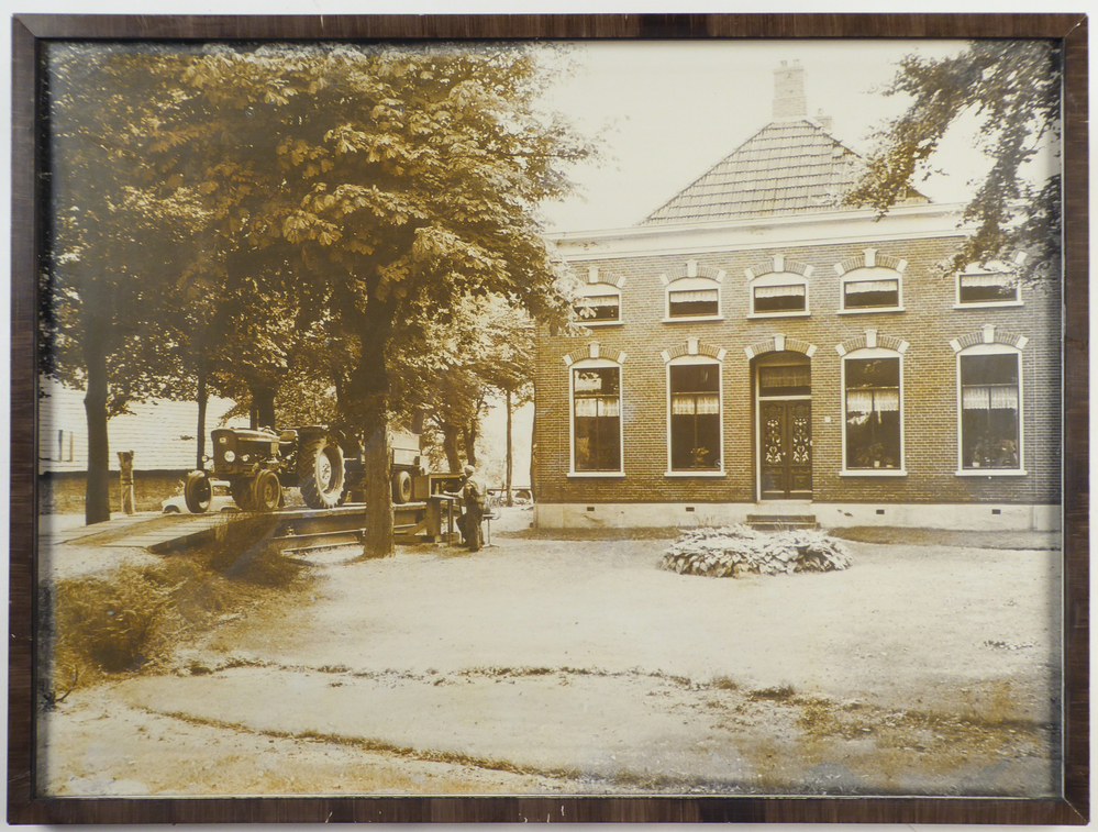 foto in houten lijst met daarop het graanpakhuis te Hellum, met rechts een tractor met kar, zonder bestuurder, die staat iets verder naar rechts bij een zittende man achter een apparaat, waarschijnlijk een weegbrug, afkomstig van de COBO ( Cooperatieve Aan- en Verkoopvereniging Boerenbelang( opgericht in 1940 als Boerenbelang G.A. te Sappemeer, in 1965 door het samengaan van Coöperatie Noord-Oost te Veendam en Coöperatie Boerenbelang te Sappemeer gefuseeerd tot COBO, fuseerde met de aankoopcentrale in 1983 tot ACECO bv, fuseerde weer in 1990 tot ACM en in 2010 tot AGRIFIRM) te Hoogezand aan de van Neckstraat.