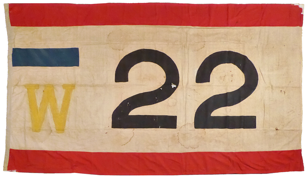 rechthoekige lap textiel van 320 cm x 190 cm, rode baan, witte baan, rode baan, met onderaan gele letter W met daarnaast zwarte cijfers 22, boven de w een blauwe balk, Kapiteinsvlag W 22 van het zeemanscollege “De Harmonie” te Wildervank van 1)Remke J. de Jonge. Hij was effectief lid van het zeemanscollege “De Harmonie” te Wildervank met vlagnummer 22 in de periode 1840 t/m 1852, daarna 2)Klaas Christiaans Kamminga W22 - Wildervank (±1860-1879) Klaas Christiaans Kamminga voer achtereenvolgens 1851-1859 op kofschip De Drie Geboeders Sikkens, en van 1860 – 1879 op de Galjoot Christina. Klaas Kamminga werd geboren 24 juli 1814 te Veendam, nabij Scholtehuizen als zoon van de bakker Christjaan Freerks Kamminga en Catharina (Kaatje Jans) Koetze (Koetse). Hij trouwde 19 december 1842 te Wildervank als zeeman met Stijntje Everts Koning, geboren te Veenam op 29 oktober 1815 als dochter van de zeeman Evert Louwes Koning en Derkje Alberts Groenewold. Stientje overleed te Appingedam op 20 juli 1894, 78 jaar. Klaas overleed 21 juni 1879 te Appingedam, 64 jaar, zonder beroep. In BS-akten van 1842 en 1844 wordt Klaas vermeld als “zeeman”, in de periode 1847 t/m 1855 als “schipper”, in 1873 als “rustend schipper” en bij zijn overlijden in 1873 als zijnde “zonder beroep”. K.C.Kamminga was effectief lid van het zeemanscollege “De Harmonie” te Wildervank met vlagnummer 73 in 1853 en met vlagnummer 22 in de periode 1860 t/m 1879. 3) De vlag is van 1897 tot en met 1903 gebruikt op de door kapitein G.H.Bakker uit Veendam bevaren zeetjalk Zwaluw. Het schip was als Johanna Frederika van stapel gelopen voor de Amsterdamse rederij G.W. Bootsma. Bakker verkocht zijn zeetjalk in 1903 aan de Groninger familie Schothorst en schonk de collegevlag in 1938 aan de Vereniging voor Veenkoloniale Oudheidkunde, de voorloper van ons museum waaruit in 1939 de stichting Veenkoloniaal Museum ontstond.