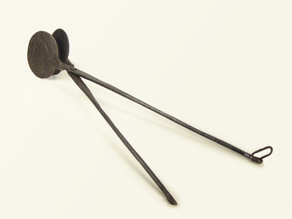 ijzeren wafelijzer met platte ronde wangen en lange steel met schakel om beide steeleinden bijeen te binden, aan binnenkant wangen gegraveerd tweeledig gekroond schild met aanweerszijde een engel en bladmotieven, in schild inscriptie : Hinderk Hinderks Trintje Wilkens, overzijde gegraveerd familiewapen, gekroond wapenschild, vastgehouden door 2 engelen, bovenste helft dolfijn met 2 sterren, onderste helft een vogel.