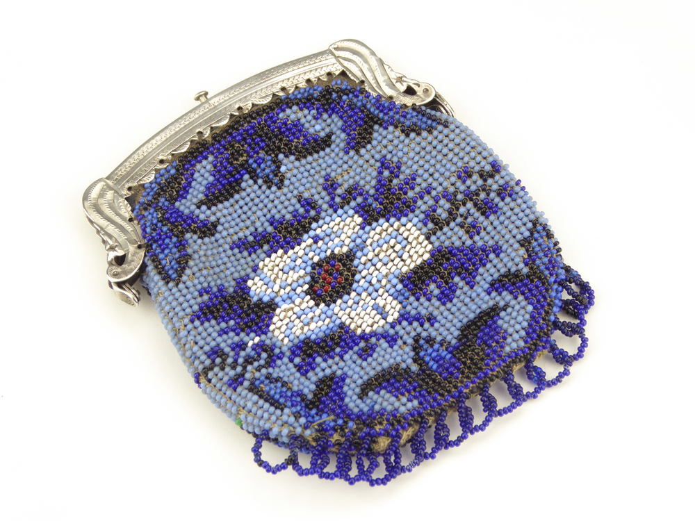 Kralenbeursje, blauwe en zwarte kralen, met in het midden een afbeelding van een witte bloem met ietwat rood zwarte kern, compleet met zilveren beugel met bladversiering, minervahoofd met M=Schoonhoven 1837-1984, jaarletter C=1862, gehalteteken leeuw 2, onduidelijk afgeslagen meestermerk, waarschijnlijk AB 17 in vierkant= Abraham Paulus Barends, werkzaam 1839 – 1891 te Hoogezand