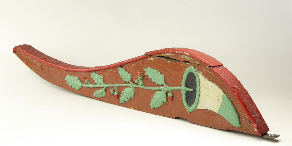 roerklik, klik: los sierstuk, op de bovenzijde van het roer bij diverse zeilschepen. Halfrond gebogen, rood van kleur met afbeelding bloemblad met rode knoppen en soort mintgroen , wit en zwarte windbuil waaruit dit ontspruit