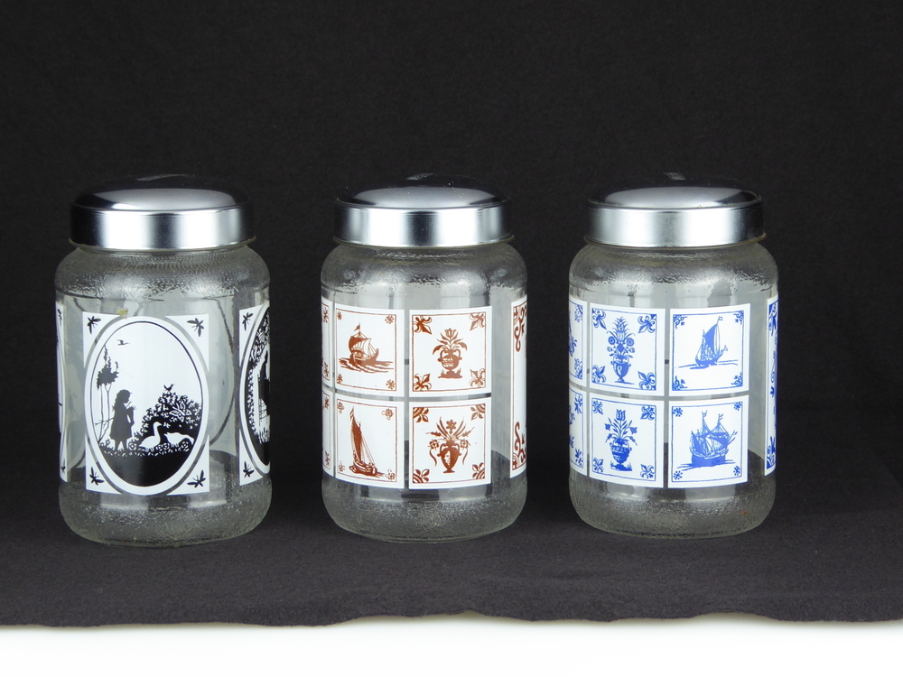 3 glazen voorraadpotten, boven en onderkant gemateerd glas, middenstuk transparant, in blikken deksel geslagen NESCAFE, rondom vinyl decoratie, respectievelijk blauwe oud hollandse wandtegels, bruine hollandse wandtegels, en zwarte knipselkunst van Wiecher Tjeerd Lever te Westerbork, ongeveer 1970