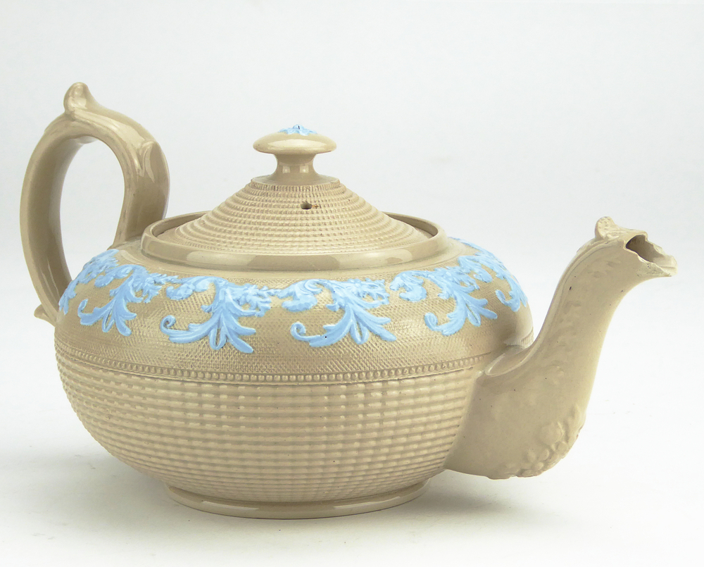 aardewerken theepot, engels, bruin met in relief blauwe geverfde bladdecor, op standvoet, met voluutoor, tuit bruin, niet geverfde bladdecoraties,onderkant geribbeld, compleet met deksel met knop, op bovenkant knop blauwe bloemdecoratie .