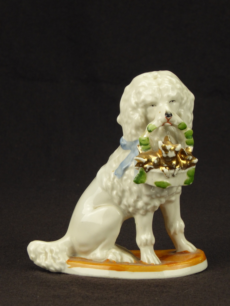 witte zittende steengoed poedel met korrelvormig lichaam, witte mand vol goudkleurige biggetjes met versiering groene blaadjes, Duits aardewerk, maar in de stijl van Staffordshire, linker model.