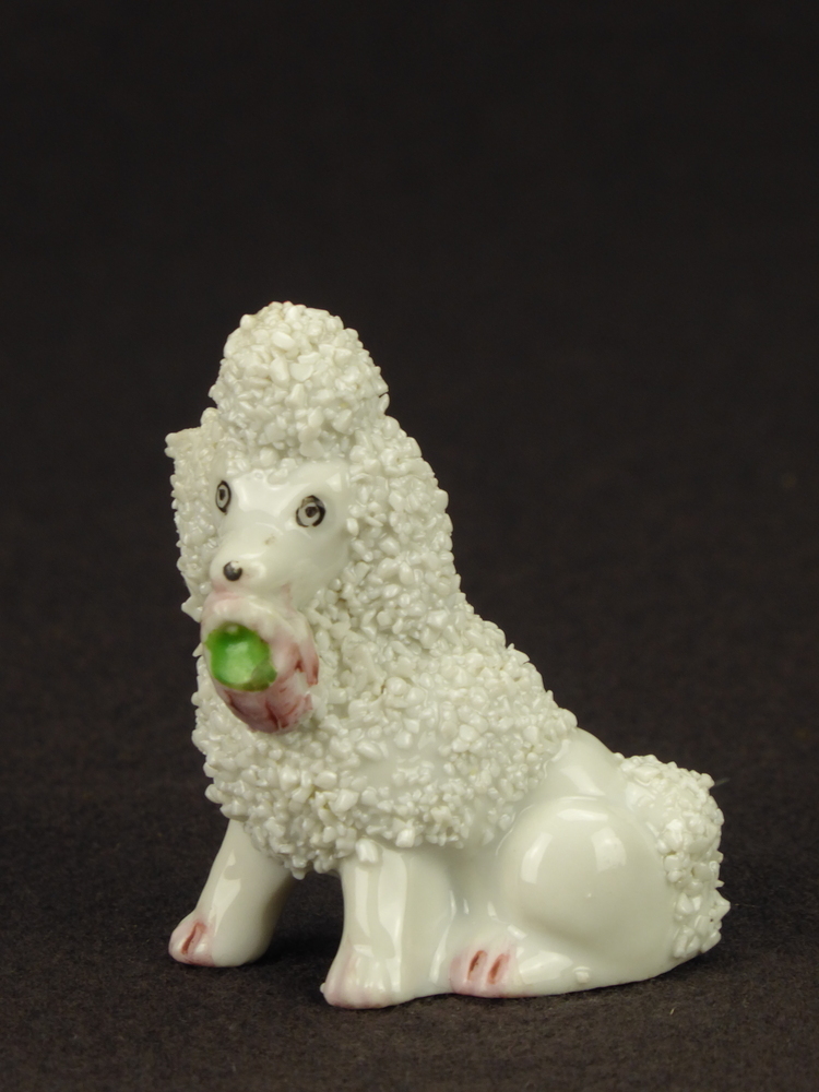 witte zittende steengoed poedel met roze mand met groene inhoud in bek, Japans aardewerk, maar in de stijl van Staffordshire, rechter model.