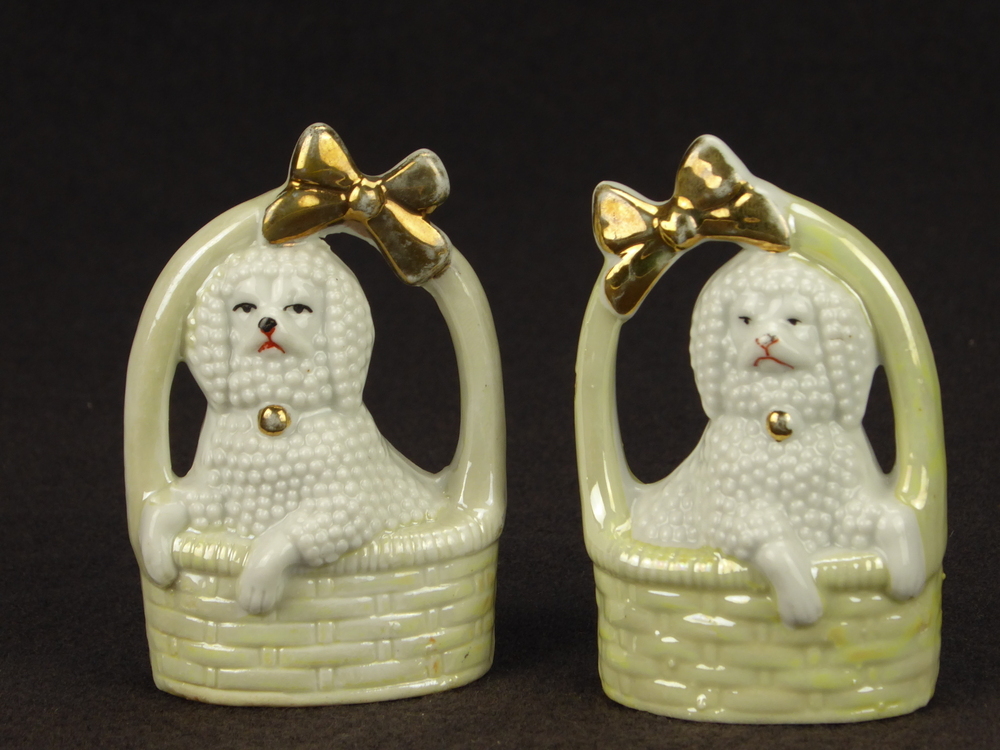 2 zittende steengoed poedels in groenige mand met poten over de rand, gouden strik aan bovenkant, linker model aan onderkant gemerkt 25