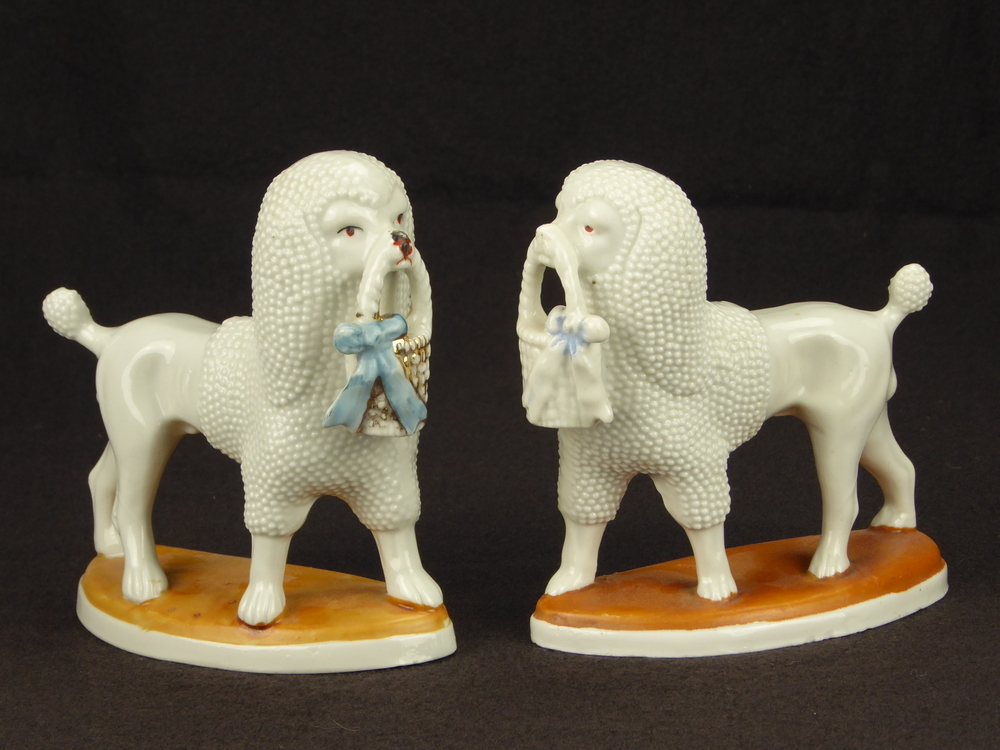 2 lopende steengoed poedels op onderplaat, met goudkleurige korf in hun bek met blauwe strik