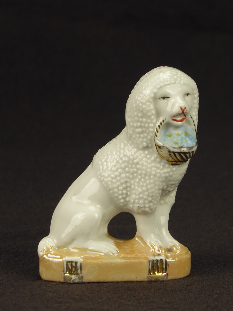 zittende steengoed poedel op bruine onderplaat met 2 goudkleurige pilaren, met goudkleurige korf met blauwe inhoud in bek