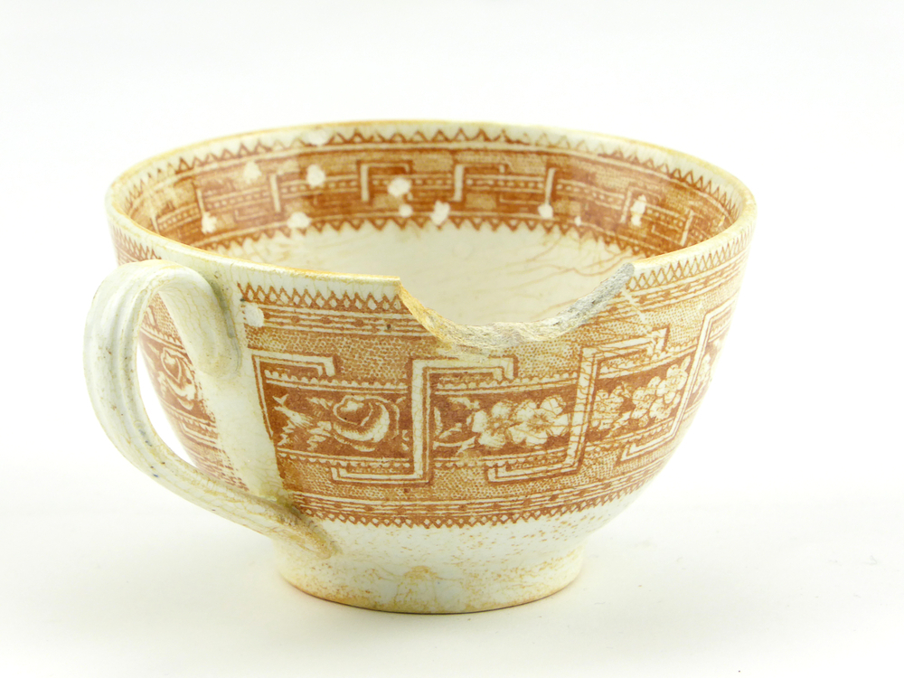 aardewerken kop van het merk Petrus Regout & Co, Maastricht, diameter 8,2 cm, op buitenkant bruine decoratie van bloemen en gestileerde wolfsangel, gemerkt met beeldmerk 71 A van Petrus Regout, opgedoken door British Sub Aqua Club, Branch 501, ook wel de 501 Divers uit Folkstone, uit het wrak van de op 19 november 1887 na een aanvaring met het stoomschip Rosa Mary gezonken stoomschip W.A. Scholten, via hun woordvoerder Glyn Jones geschonken aan het Veenkoloniaal Museum.