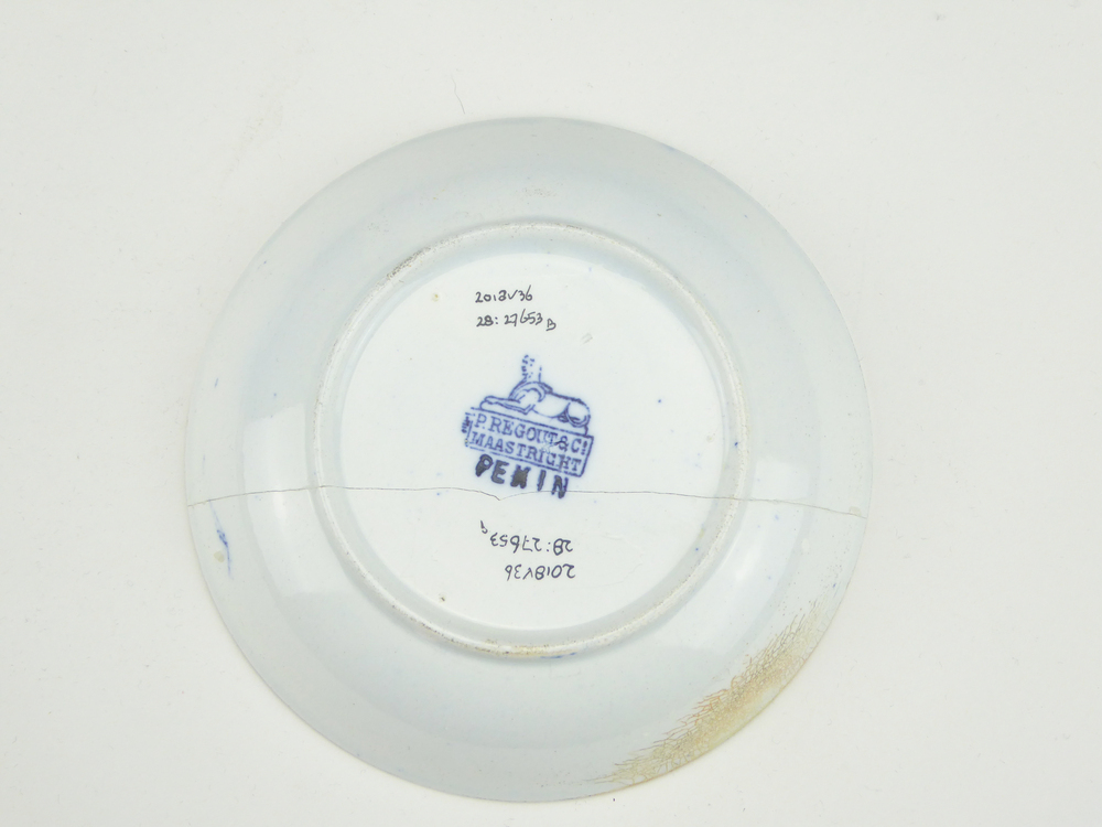 aardewerken schotel van het merk Petrus Regout & Co, Maastricht, schotel diameter 13,5 cm, op binnenkant blauw decoratie van bloemen, bomen, een man op een loopbrug loopt langs een zittende man, op de achtergrond een pagode, schotel gemerkt met beeldmerk 71 A van Petrus Regout, schotel decornaam Pekin, opgedoken door British Sub Aqua Club, Branch 501, ook wel de 501 Divers uit Folkstone, uit het wrak van de op 19 november 1887 na een aanvaring met het stoomschip Rosa Mary gezonken stoomschip W.A. Scholten, via hun woordvoerder Glyn Jones geschonken aan het Veenkoloniaal Museum.