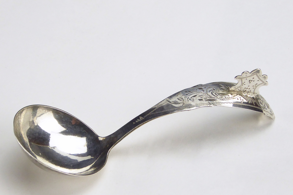 roomlepeltje. De steel is gebogen en heeft een mooie fijne bloemdecoratie. Steel gedecoreerd met een opstaand kammetje. Op de achterkant van het roomlepeltje zit een haakje. Meesterteken: G 5 = Willem Hermannus Groenier (Veendam) meestertekens 1848 - 1890 Jaarletter:B= 1886 Gehalteteteken leeuw 2 Lengte: 11 cm