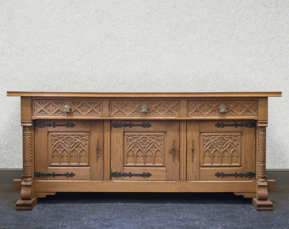 eikenhouten kast, langwerpig met 3 rijkelijk versierde kastdeuren met ijzeren beslag, binnenkant vakverdeling in 2 stukken, zijkanten van de kast bestaan uit zuilen met diagonale inkepingen uitmondende in een groter onderstuk, erboven 3 lades met messing deurknop in de vorm van een gezicht.