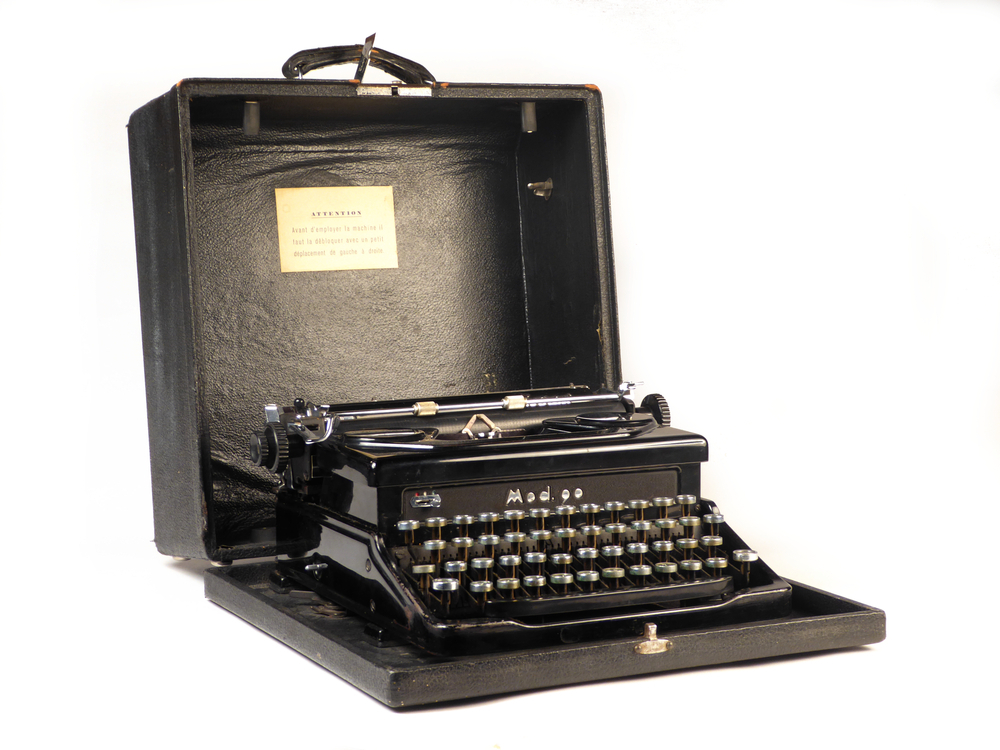 zwarte ijzeren typemachine in hout met leer omtrokken koffer met hengsel, slot aan voorkant gegraveerd Everest, slot moet eerst opengeklapt, dan palletje naar beneden om bovenkant geheel los te doen van onderplaat met typemachine, mod .90 serienummer 177567. Schenkster werkte vanaf 1967 bij W.A. Scholten. Toen het bedrijf omstreeks 1978 / 1979 Avebe werd, nam zij de typemachine mee naar huis.