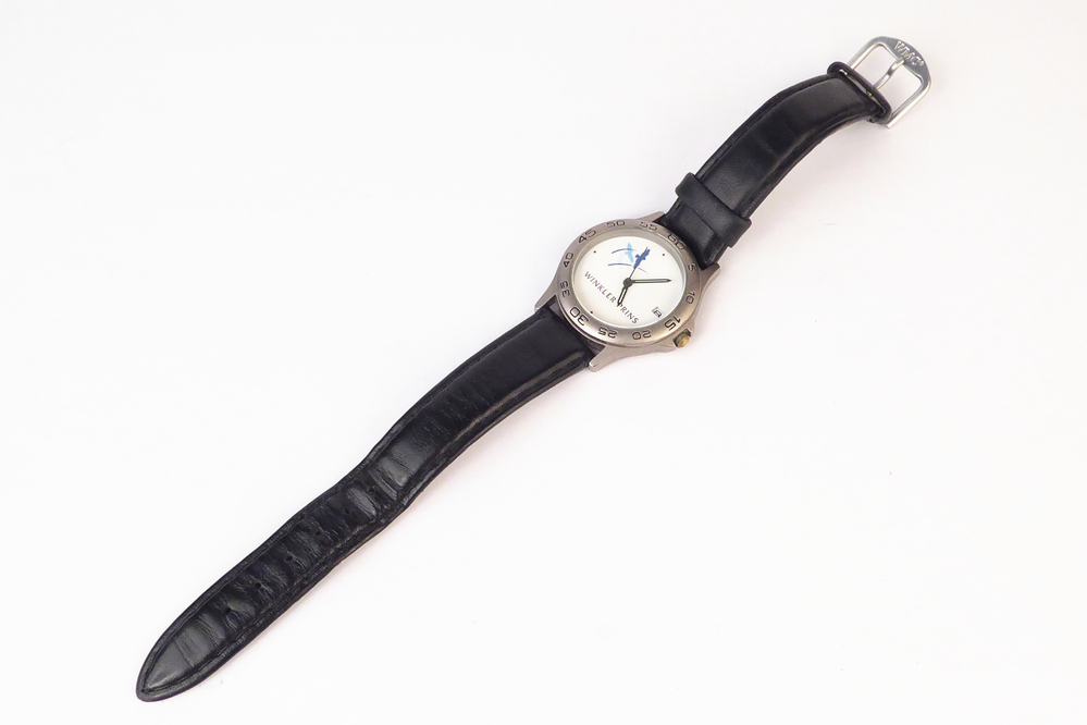 non ferro metalen horloge met lederen band, rondom rand schaalverdeling 0 - 60, op wijzerplaat Winkler prins. Volgens ingewijde kreeg iedereen bij een jubileum van de Winkler Prins School zo'n horloge, volgens schenker kregen kinderen er een zodat ze op tijd op school aanwezig konden zijn.