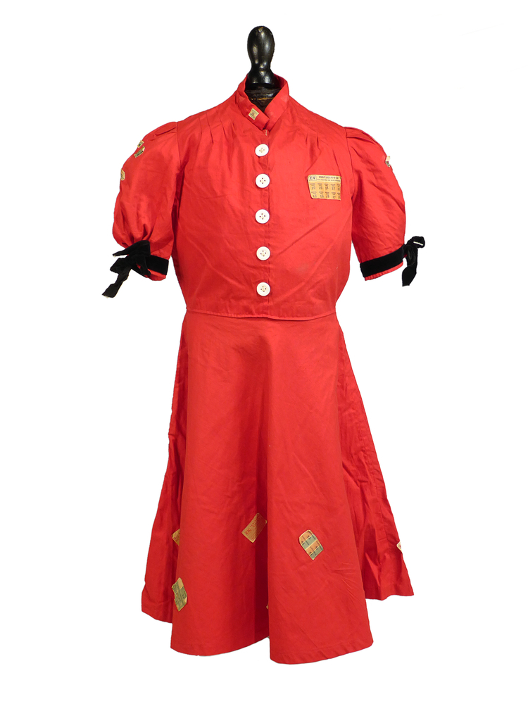 rode katoenen jurk met witte knopen, zitten er voor de sier op want de sluiting is met haken en ogen, buitenkant beplakt met distributiebonnen, gebruikt door schenker G.M. Abeling. Geziena Maria Anna Abeling werd 4 september 1922 te Oude Pekela geboren als dochter van Bernhardus Johannes Josephus Abeling en Catharina Gesina Hensen. Haar ouders hadden een manufacturenzaak aan de Hendrik Westerstraat 471 te Oude Pekela met de naam "Hebo". De jurk werd gedragen na WW II, tijdens het carnaval in 1946.