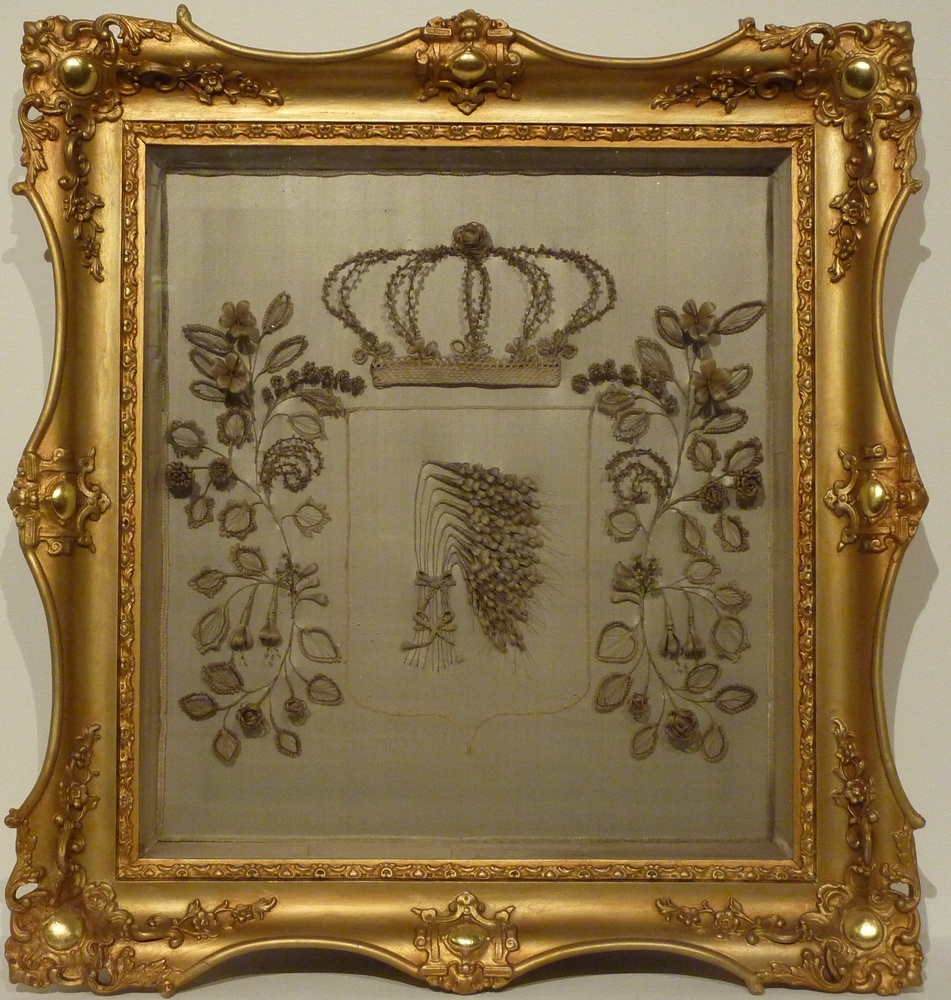 haarschilderij met familiewapen Sannes, gemaakt van haar van overleden kind. gevlochten van haar van schoonouders en hun kinderen. Een staande korenschoof met boven een kroon, aan weerszijden geflankeerd door een ornament.