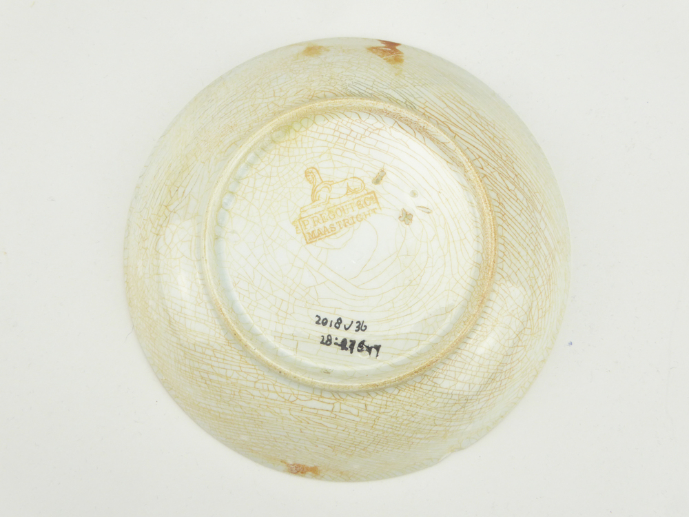 aardewerken schotel van het merk Petrus Regout & Co, Maastricht, diameter 13,5 cm, op binnenkant donkergeel tegen oranje aan gekleurde decoratie van florale motieven, gemerkt met beeldmerk 71 A van Petrus Regout, blindmerk kruisje en streepje, opgedoken door British Sub Aqua Club, Branch 501, ook wel de 501 Divers uit Folkstone, uit het wrak van de op 19 november 1887 na een aanvaring met het stoomschip Rosa Mary gezonken stoomschip W.A. Scholten, via hun woordvoerder Glyn Jones geschonken aan het Veenkoloniaal Museum.