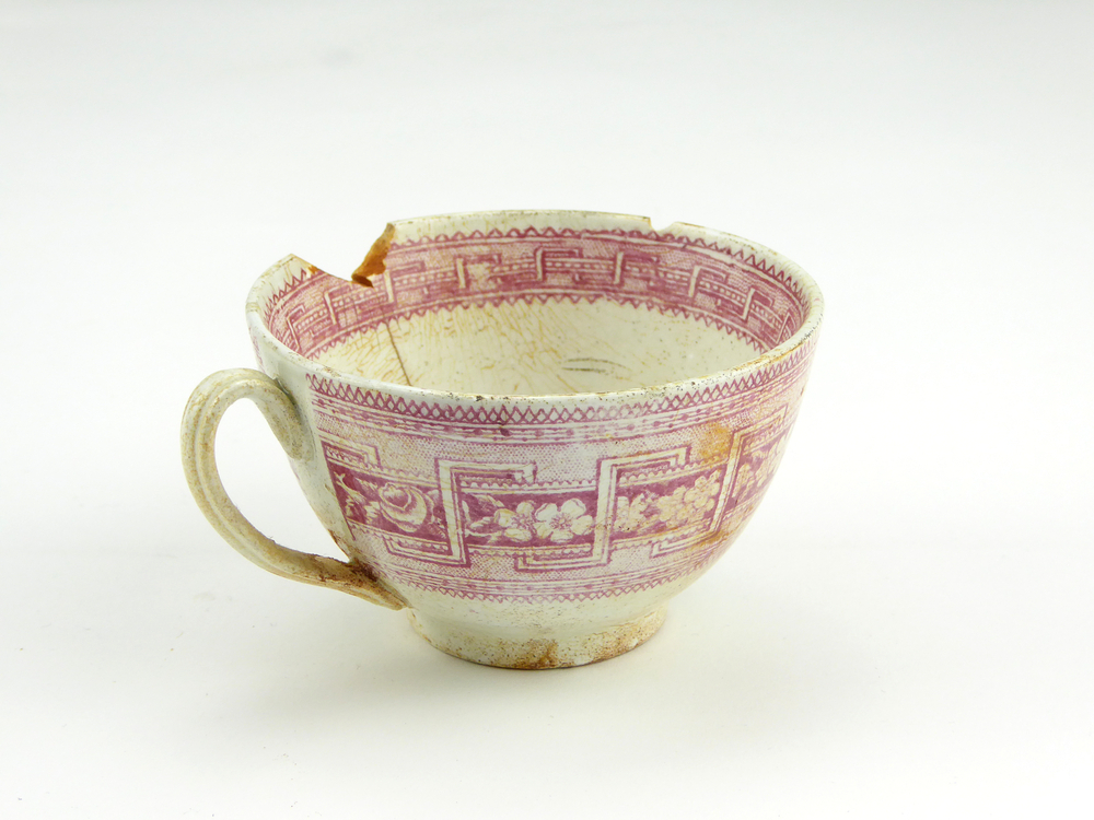 aardewerken kop van het merk Petrus Regout & Co, Maastricht, diameter 8,2 cm, op buitenkant rode decoratie van bloemen en gestileerde wolfsangel, gemerkt met beeldmerk 71 A van Petrus Regout, opgedoken door British Sub Aqua Club, Branch 501, ook wel de 501 Divers uit Folkstone, uit het wrak van de op 19 november 1887 na een aanvaring met het stoomschip Rosa Mary gezonken stoomschip W.A. Scholten, via hun woordvoerder Glyn Jones geschonken aan het Veenkoloniaal Museum.