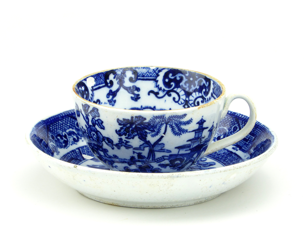 aardewerken kop en schotel van het merk Petrus Regout & Co, Maastricht, kop diameter 8 cm, schotel diameter 13,5 cm, op buiten en binnenkant blauw decoratie van bloemen, bomen, een man op een loopbrug loopt langs een zittende man, op de achtergrond een pagode, schotel binnenkant blauwe decoratie boom, boot, hek gebouw, gemerkt met beeldmerk 71 A van Petrus Regout, schotel decornaam Willow, opgedoken door British Sub Aqua Club, Branch 501, ook wel de 501 Divers uit Folkstone, uit het wrak van de op 19 november 1887 na een aanvaring met het stoomschip Rosa Mary gezonken stoomschip W.A. Scholten, via hun woordvoerder Glyn Jones geschonken aan het Veenkoloniaal Museum.