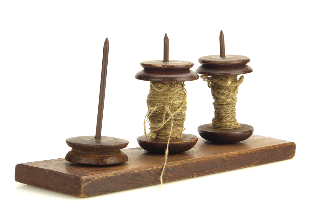 langwerpige houten plank met daarop 3 horizonaal geplaatste ijzeren pennen, op twee daarvan zit een klos met houten boven en onderkant, bespannen met touw, en een losse houten ronde schijf