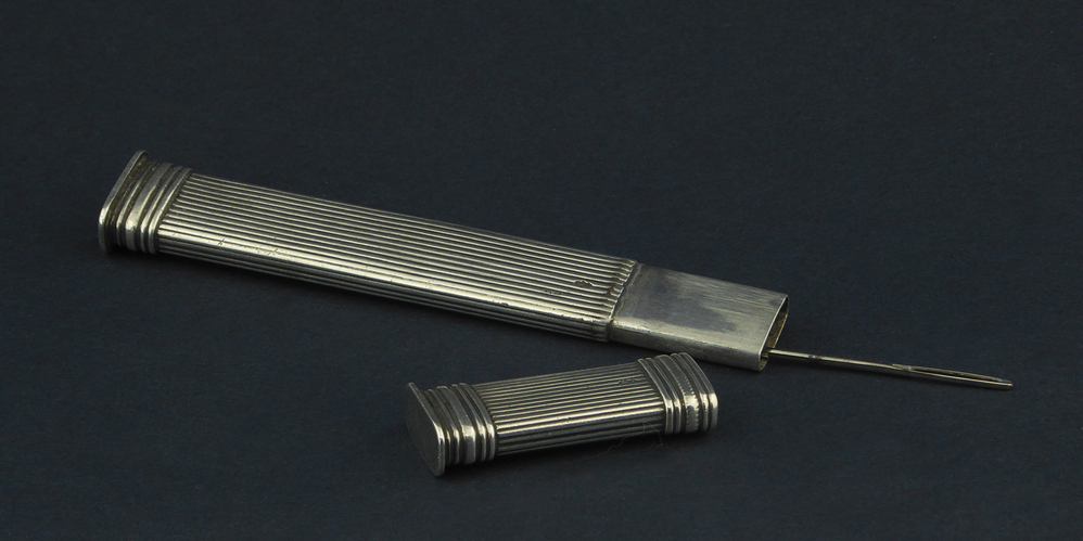 langwerpige zuilvormige zilveren naaldenkoker, aan zijkant gemerkt JVD = Jan Hendrik van Denderen, zilversmid werkzaam te Wildervank, geboren 8 mrt 1842 te Winschoten, overleden 22 sep 1904 te Groningen, beroep(en): goud-en zilverwerker, Gehuwd 16 nov 1865 te Wildervank met: Renske Stijntjes, geboren 8 jun 1841 te Stadskanaal, overleden 5 mrt 1896 te Helpman, merk gebruikt tussen 1878 - 1891. Onderop bodem gegraveerd E v O, waarschijnlijk Eiske van Oosten, dienstmeid, geboren 29 augustus 1834 te Bedum,  gehuwd 14 februari 1857 te Bedum 1) met Gerard Bodewes, gehuwd 20 februari 1878 te Wildervank 2) met Menno Wildervank