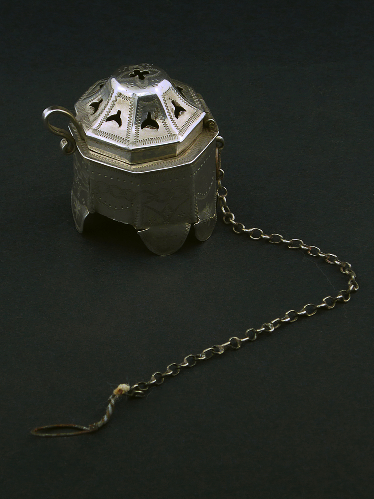 zilveren kap met oortje en scharnier, diameter 3 cm, hoogte 3,5 cm, bovenkant deksel heeft 8 sikkelvormige gaten en in het midden kruisvormig gat, aan een 14 cm lange ijzeren ketting, vuurklep voor pijp, aan zijkant gemerkt met een zwaardje, keurmerk voor klein zilverwerk, gebruikt tussen 1858 en 1906.