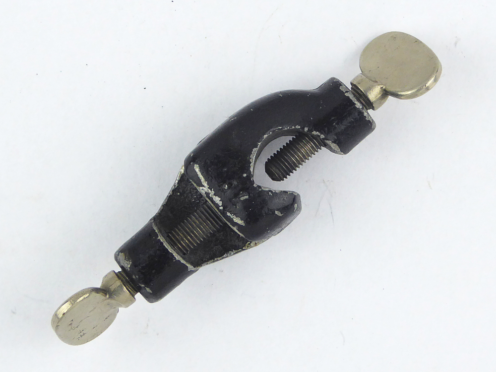 zwarte nikkelen in het midden bolle behuizing, waar aan weerszijden iets scheef en haaks van elkaar een uitsparing is gemaakt, welke om een statiefstang kan vallen, met aan de zijkant een schroef om iets vast te zetten hieraan en aan de statiefstang