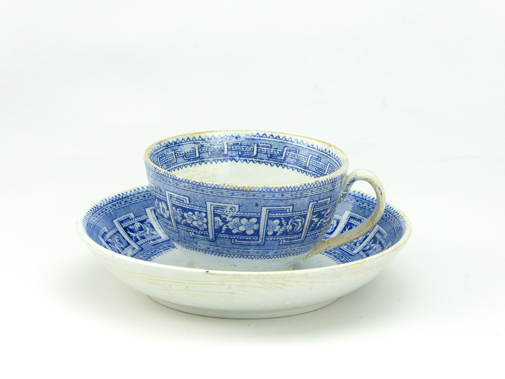 aardewerken kop en schotel van het merk Petrus Regout & Co, Maastricht, kop diameter 8 cm, schotel diameter 13,5 cm, op buiten en binnenkant blauwe decoratie van bloemen en wolfsangel, blindmerk 4, gemerkt met beeldmerk 71 A van Petrus Regout, schotel decornaam Border, opgedoken door British Sub Aqua Club, Branch 501, ook wel de 501 Divers uit Folkstone, uit het wrak van de op 19 november 1887 na een aanvaring met het stoomschip Rosa Mary gezonken stoomschip W.A. Scholten, via hun woordvoerder Glyn Jones geschonken aan het Veenkoloniaal Museum.