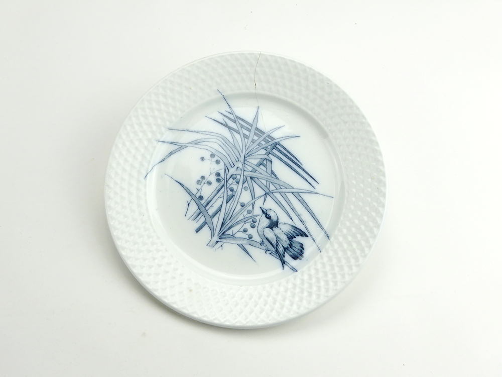 aardewerken ontbijtbordje van het merk Petrus Regout & Co, Maastricht, decornaam Plate, diameter 18 cm, op voorkant blauwe decoratie van vogel op tak met lijsterbestakjes, aan achterkant gemerkt met beeldmerk 71 A van Petrus Regout, blindmerk 6 en G, opgedoken door British Sub Aqua Club, Branch 501, ook wel de 501 Divers uit Folkstone, uit het wrak van de op 19 november 1887 na een aanvaring met het stoomschip Rosa Mary gezonken stoomschip W.A. Scholten, via hun woordvoerder Glyn Jones geschonken aan het Veenkoloniaal Museum.