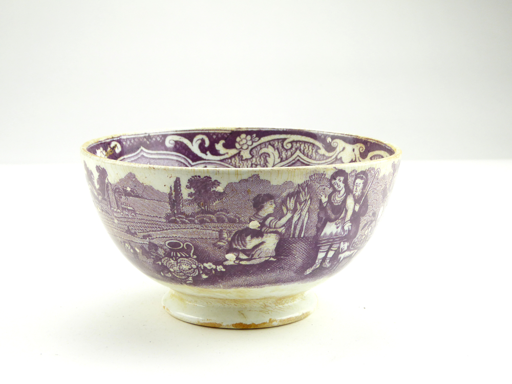 aardewerken kom op standvoet van het merk Petrus Regout & Co, Maastricht, decornaam Ruth Boaz, diameter 14,9 cm, op buitenkant paarsrode decoratie van het bijbelverhaal Ruth en Boaz, een vrouw zit aren te rapen, rechts naast haar een herder en een rijke man met omslagdoek, op de achtergrond is iemand bezig op een akker, en er staat een kerkje op de achtergrond, gemerkt met beeldmerk 71 A van Petrus Regout, opgedoken door British Sub Aqua Club, Branch 501, ook wel de 501 Divers uit Folkstone, uit het wrak van de op 19 november 1887 na een aanvaring met het stoomschip Rosa Mary gezonken stoomschip W.A. Scholten, via hun woordvoerder Glyn Jones geschonken aan het Veenkoloniaal Museum.