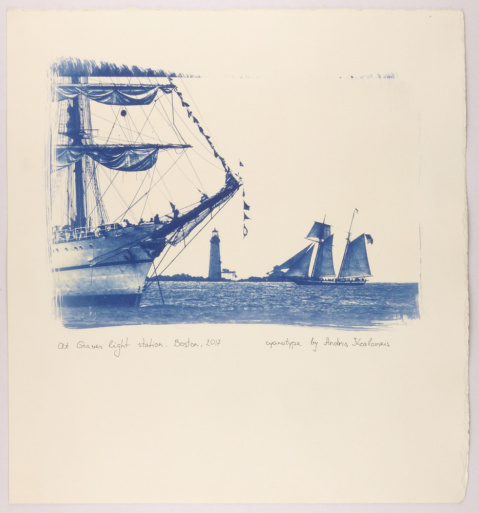 cyanotype foto afgedrukt op aquarelpapier geheel in het blauw met een afbeelding van twee achter elkaar liggende zeilschepen met een vuurtoren, onder afdruk met zwarte pen geschreven : at graves light station cyanotype by Andris Koslovskis