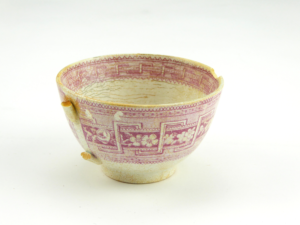 aardewerken kop van het merk Petrus Regout & Co, Maastricht, diameter 8,2 cm, op buitenkant rode decoratie van bloemen en gestileerde wolfsangel, gemerkt met beeldmerk 71 A van Petrus Regout, opgedoken door British Sub Aqua Club, Branch 501, ook wel de 501 Divers uit Folkstone, uit het wrak van de op 19 november 1887 na een aanvaring met het stoomschip Rosa Mary gezonken stoomschip W.A. Scholten, via hun woordvoerder Glyn Jones geschonken aan het Veenkoloniaal Museum.