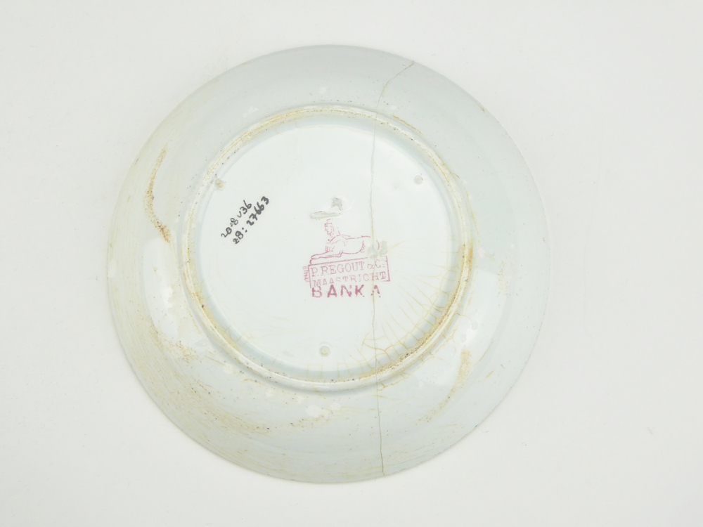 aardewerken schotel van het merk Petrus Regout & Co, Maastricht, schotel diameter 13,5 cm, op binnenkant rode decoratie van bloemen en bloemenvaas, blindmerk 4, gemerkt met beeldmerk 71 A van Petrus Regout, schotel decornaam Banka, opgedoken door British Sub Aqua Club, Branch 501, ook wel de 501 Divers uit Folkstone, uit het wrak van de op 19 november 1887 na een aanvaring met het stoomschip Rosa Mary gezonken stoomschip W.A. Scholten, via hun woordvoerder Glyn Jones geschonken aan het Veenkoloniaal Museum.