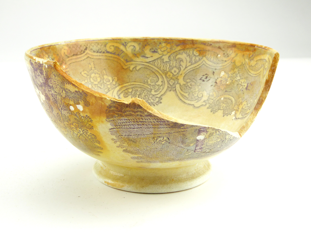 aardewerken kom op standvoet van het merk Petrus Regout & Co, Maastricht, decornaam Ruth Boaz, diameter 14,9 cm, op buitenkant paarsrode decoratie van het bijbelverhaal Ruth en Boaz, een vrouw zit aren te rapen, rechts naast haar een herder en een rijke man met omslagdoek, op de achtergrond is iemand bezig op een akker, en er staat een kerkje op de achtergrond, gemerkt met beeldmerk 71 A van Petrus Regout, dikke scherf uit zijkant en losse scherf, opgedoken door British Sub Aqua Club, Branch 501, ook wel de 501 Divers uit Folkstone, uit het wrak van de op 19 november 1887 na een aanvaring met het stoomschip Rosa Mary gezonken stoomschip W.A. Scholten, via hun woordvoerder Glyn Jones geschonken aan het Veenkoloniaal Museum.