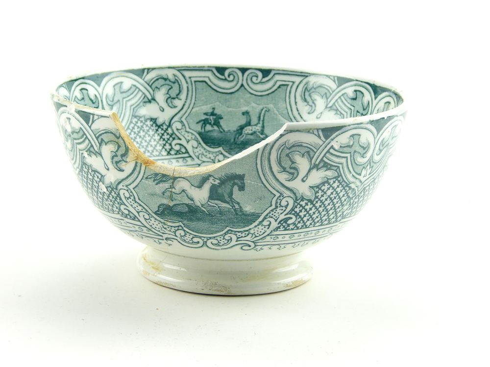 aardewerken kom op standvoet van het merk Petrus Regout & Co, Maastricht, decornaam Lasso, diameter 14,9 cm, op binnenkant 4 x groene decoratie van man op paard met lasso die paarden vangt, buitenkant groene decoratie van loslopende paarden en man op paard met lasso, dikke scherf uit zijkant, gemerkt met beeldmerk 71 A van Petrus Regout, opgedoken door British Sub Aqua Club, Branch 501, ook wel de 501 Divers uit Folkstone, uit het wrak van de op 19 november 1887 na een aanvaring met het stoomschip Rosa Mary gezonken stoomschip W.A. Scholten, via hun woordvoerder Glyn Jones geschonken aan het Veenkoloniaal Museum.