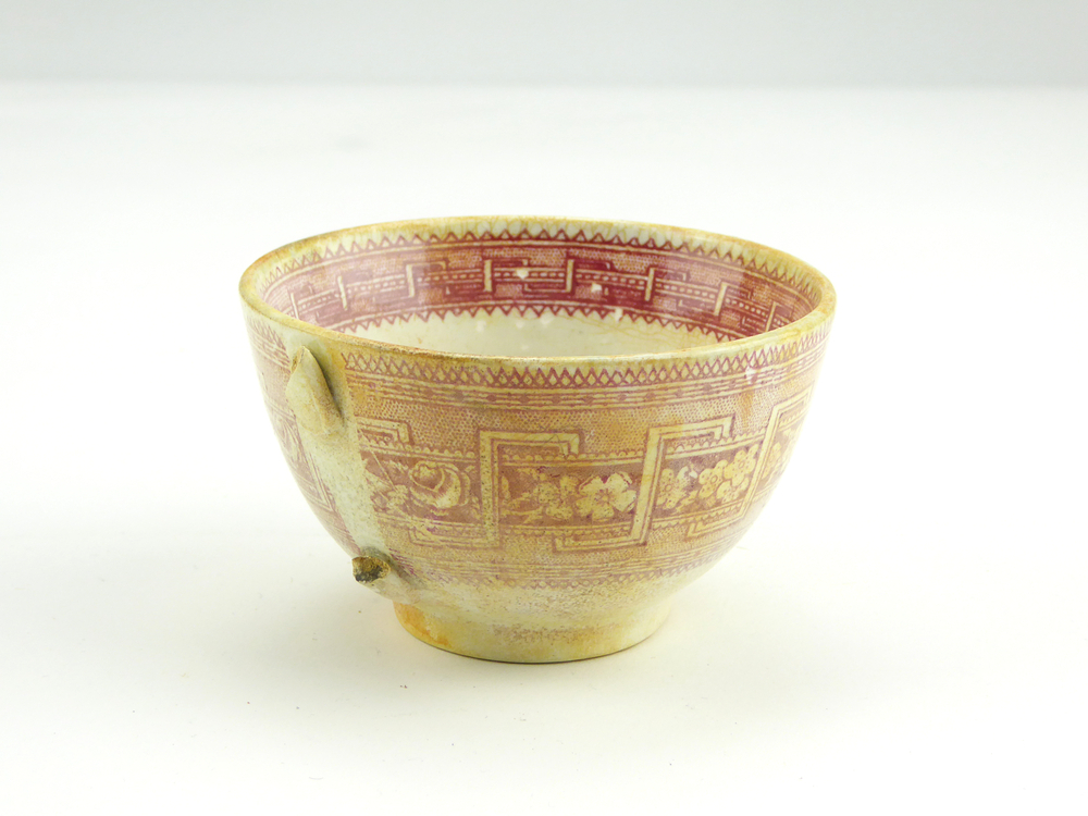 aardewerken kop van het merk Petrus Regout & Co, Maastricht, diameter 8,2 cm, op buitenkant rode decoratie van bloemen en gestileerde wolfsangel, gemerkt met beeldmerk 71 A van Petrus Regout, opgedoken door British Sub Aqua Club, Branch 501, ook wel de 501 Divers uit Folkstone, uit het wrak van de op 19 november 1887 na een aanvaring met het stoomschip Rosa Mary gezonken stoomschip W.A. Scholten, via hun woordvoerder Glyn Jones geschonken aan het Veenkoloniaal Museum.