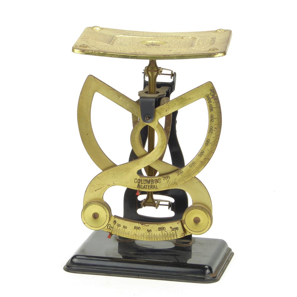 metalen weegschaal met opzij bewegende halve cirkelvormige armen en bovenop een messingkleurige weegblad met inscriptie niet voor handelsdoeleinden en aan voorkant inscriptie op weegarmen Columbus Bilateral