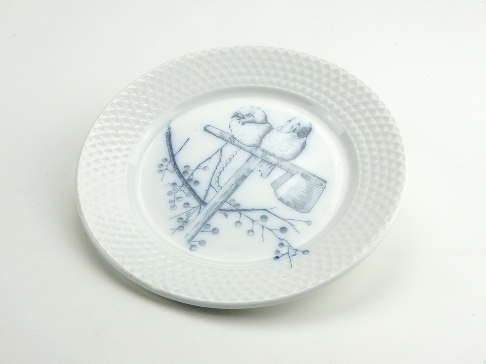 aardewerken ontbijtbordje van het merk Petrus Regout & Co, Maastricht, decornaam Plate, diameter 18 cm, op voorkant blauwe decoratie van 2 vogels op een t vormige stok met aan uiteinde 2 voerbakjes, onder zijn lijsterbestakjes te zien, aan achterkant gemerkt met beeldmerk 71 A van Petrus Regout, blindmerk 6 en G, opgedoken door British Sub Aqua Club, Branch 501, ook wel de 501 Divers uit Folkstone, uit het wrak van de op 19 november 1887 na een aanvaring met het stoomschip Rosa Mary gezonken stoomschip W.A. Scholten, via hun woordvoerder Glyn Jones geschonken aan het Veenkoloniaal Museum.