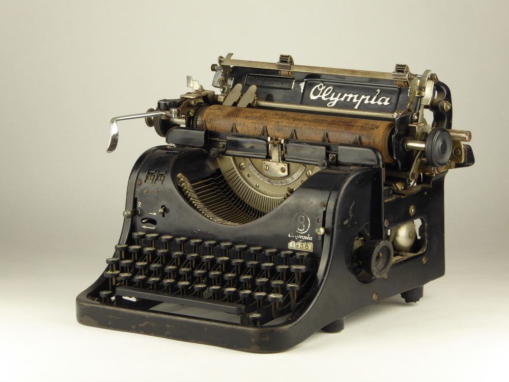 rechthoekige metalen constructie met zwarte toetsen op metalen pennetjes, houtkleurige rol voor doorvoer papier en hendel om gehele rol naar links of rechts te bewegen, op bovenkant merk Olympia